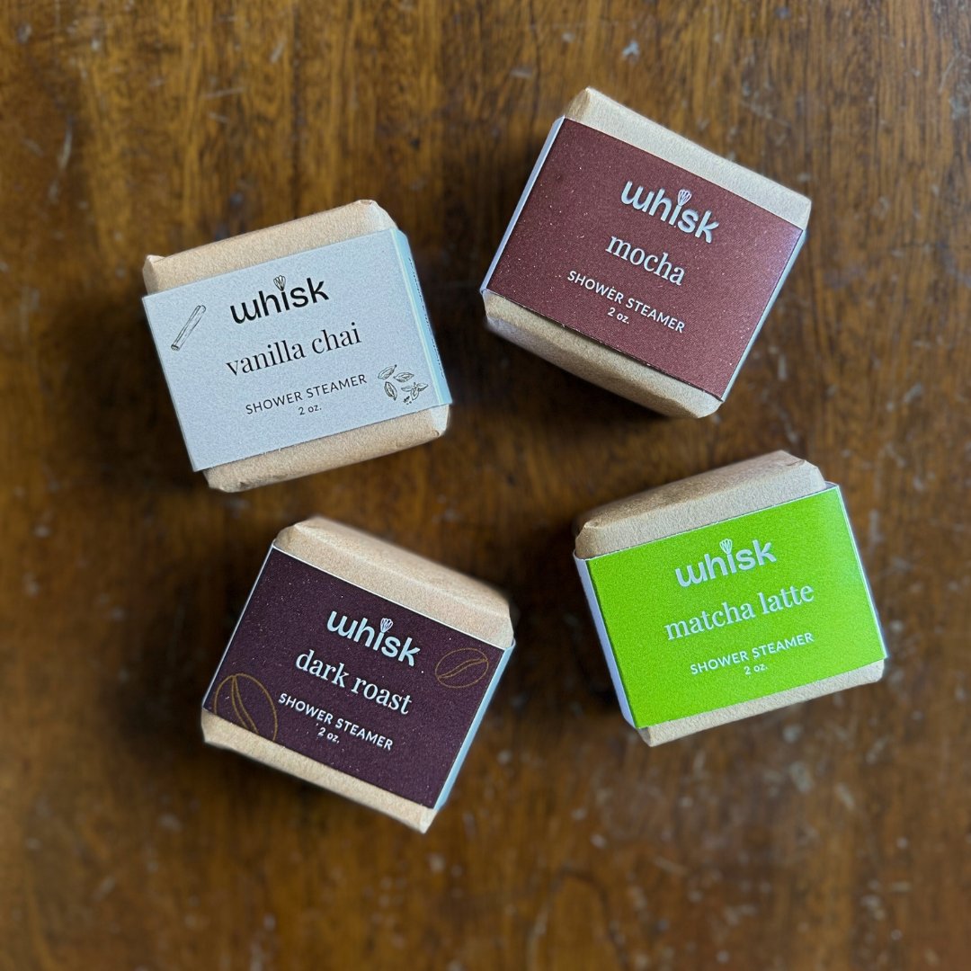 Four Whisk shower steamers on a wooden surface