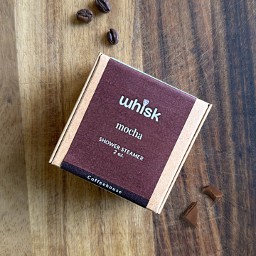 Whisk Mocha shower steamer on a wooden surface with coffee beans and chocolate pieces.